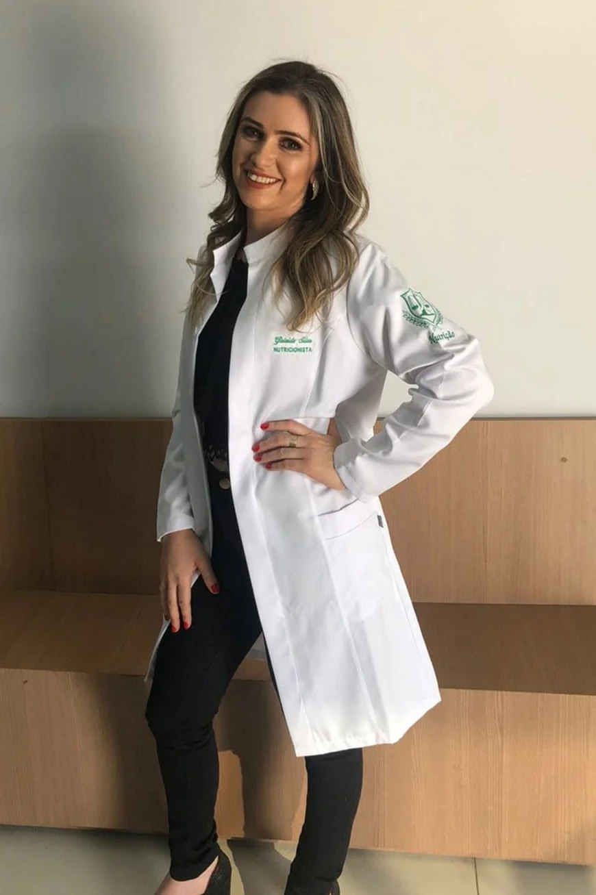 Gisleide Silva sorrindo, de jaleco branco bordado com o nome dela
